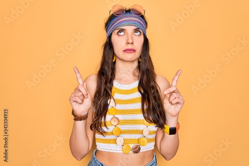 Young beautiful hippie woman with blue eyes wearing accesories and sunnglasses Pointing up looking sad and upset, indicating direction with fingers, unhappy and depressed.