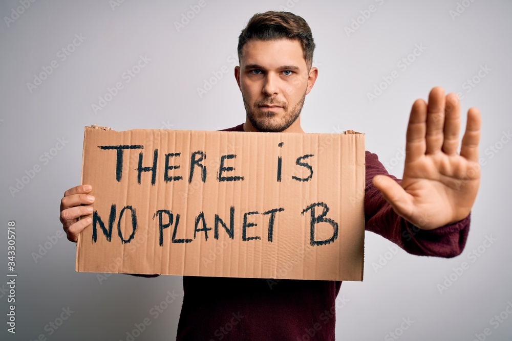 Young activist man holding protest banner for climate change and environment change with open hand doing stop sign with serious and confident expression, defense gesture Young activist man holding protest banner for climate change and environment change with open hand doing stop sign with serious and confident expression, defense gesture