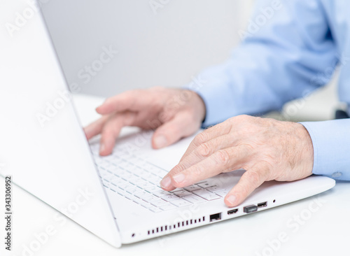 Fototapeta Naklejka Na Ścianę i Meble -  Elderly person works on laptop in a office