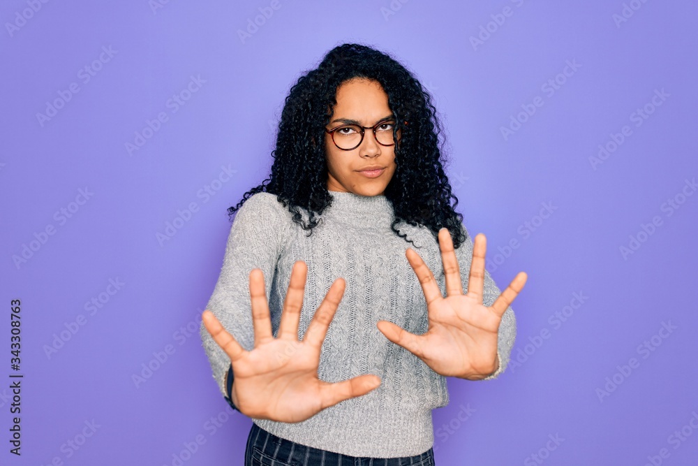 Young african american woman wearing casual sweater and glasses over purple background afraid and terrified with fear expression stop gesture with hands, shouting in shock. Panic concept.
