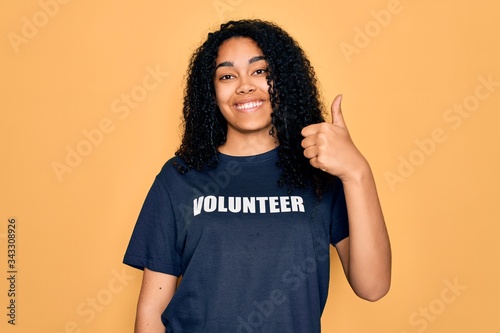 Young african american curly woman doing volunteering wearing volunteer t-shirt happy with big smile doing ok sign, thumb up with fingers, excellent sign photo
