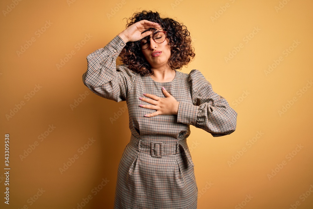 Beautiful arab business woman wearing dress and glasses standing over yellow background Touching forehead for illness and fever, flu and cold, virus sick Beautiful arab business woman wearing dress and glasses standing over yellow background Touching forehead for illness and fever, flu and cold, virus sick