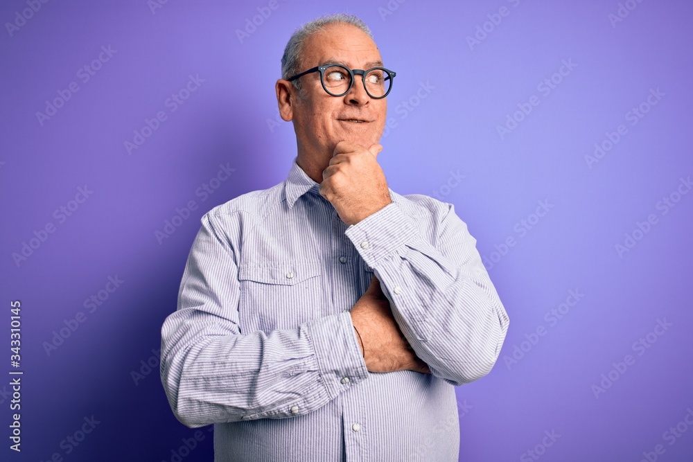 Middle age handsome hoary man wearing striped shirt and glasses over purple background with hand on chin thinking about question, pensive expression. Smiling with thoughtful face. Doubt concept. Middle age handsome hoary man wearing striped shirt and glasses over purple background with hand on chin thinking about question, pensive expression. Smiling with thoughtful face. Doubt concept.