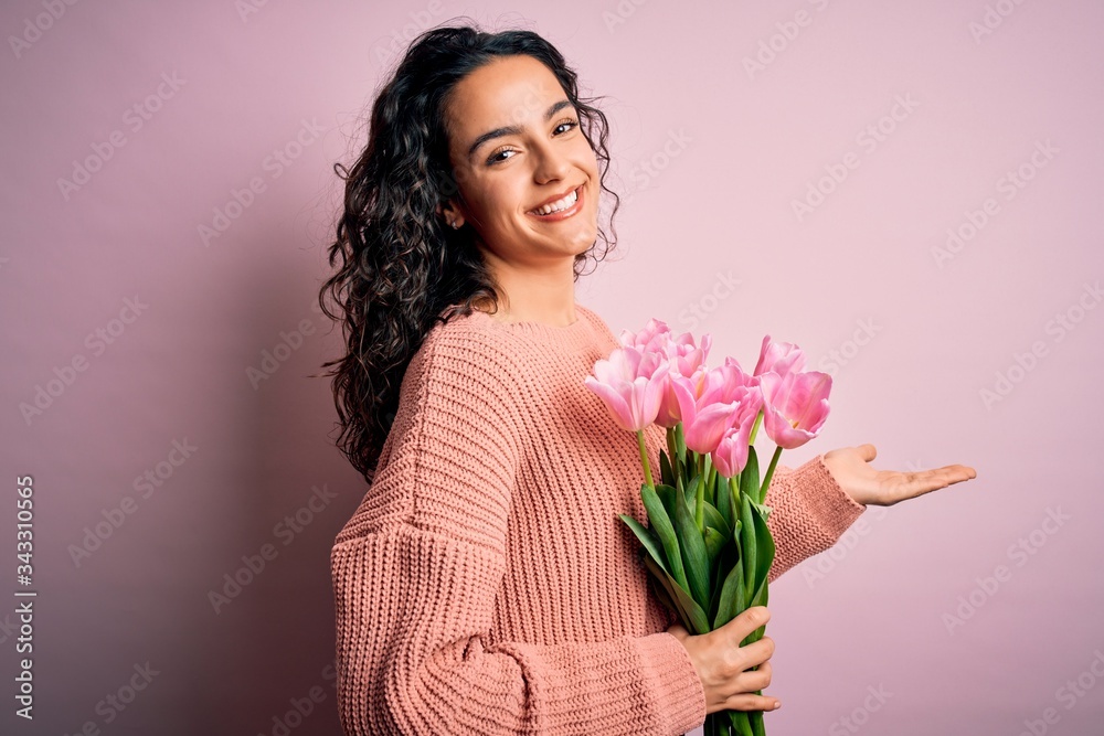 Young beautiful romantic woman with curly hair holding bouquet of pink tulips pointing aside with hands open palms showing copy space, presenting advertisement smiling excited happy Young beautiful romantic woman with curly hair holding bouquet of pink tulips pointing aside with hands open palms showing copy space, presenting advertisement smiling excited happy
