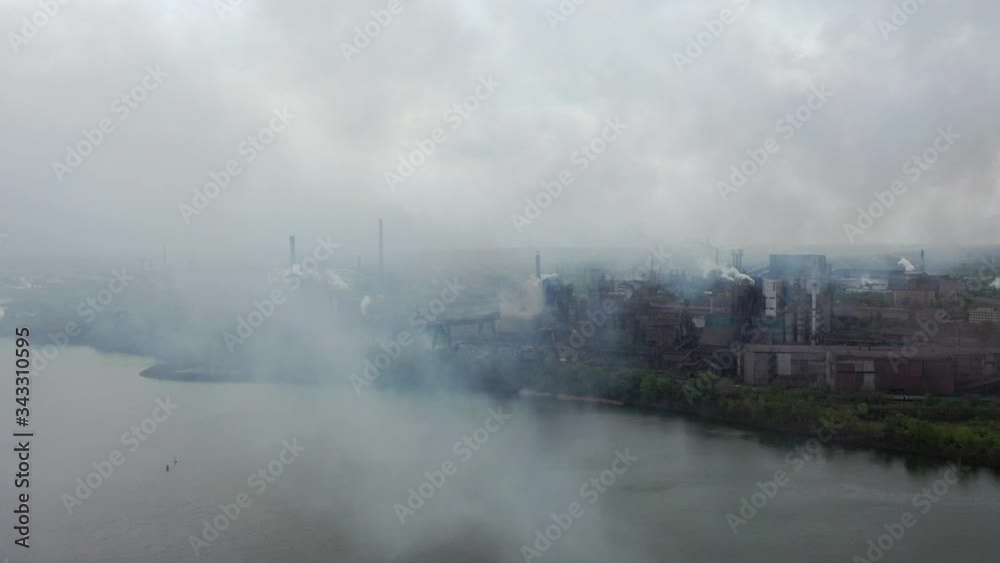 View of industrial factories and plants through puffs of smoke emitted from high pipes into air. environmental pollution by heavy industry metallurgy, chemical production. rusty pipes, tanks, cranes View of industrial factories and plants through puffs of smoke emitted from high pipes into air. environmental pollution by heavy industry metallurgy, chemical production. rusty pipes, tanks, cranes