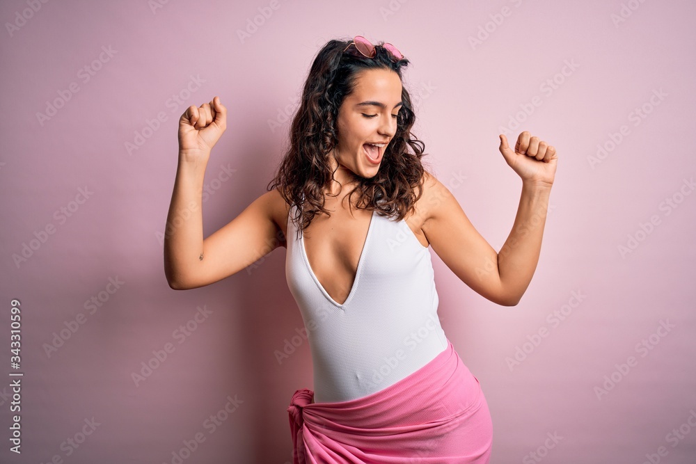 Beautiful woman with curly hair on vacation wearing white swimsuit over pink background Dancing happy and cheerful, smiling moving casual and confident listening to music Beautiful woman with curly hair on vacation wearing white swimsuit over pink background Dancing happy and cheerful, smiling moving casual and confident listening to music