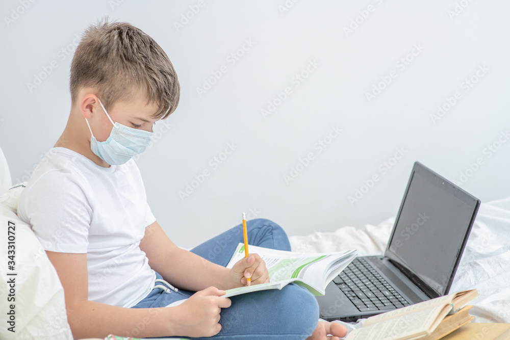 Smart boy wearing medical mask is engaged in distance learning with a laptop. Quarantine and coronavirus epidemic concept