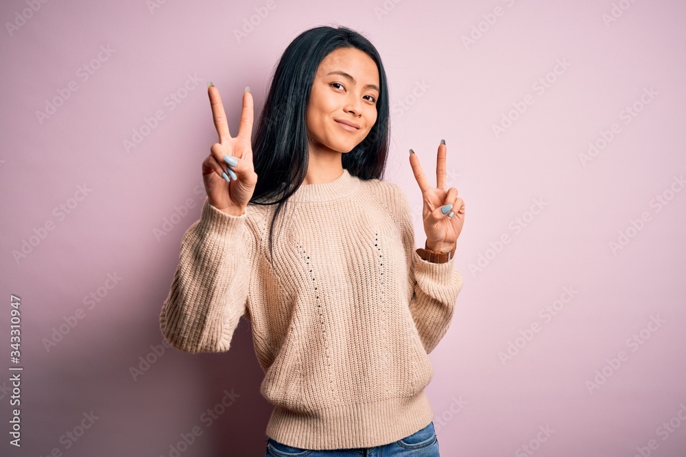 Young beautiful chinese woman wearing casual sweater over isolated pink background smiling looking to the camera showing fingers doing victory sign. Number two. Young beautiful chinese woman wearing casual sweater over isolated pink background smiling looking to the camera showing fingers doing victory sign. Number two.