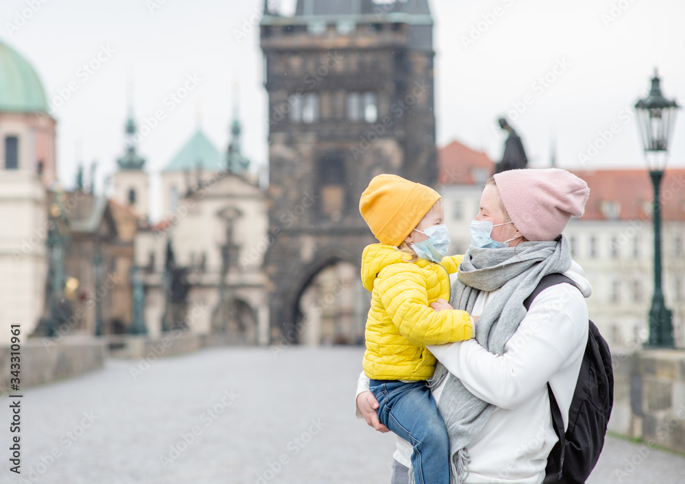 Mother and her little daughter wearing medical masks on Charles Bridge in Prague. Coronavirus epidemic concept. Empty space for text Mother and her little daughter wearing medical masks on Charles Bridge in Prague. Coronavirus epidemic concept. Empty space for text