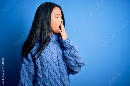 Young beautiful chinese woman wearing casual sweater over isolated blue background bored yawning tired covering mouth with hand. Restless and sleepiness.