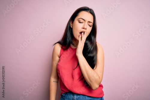 Young brunette woman wearing casual summer shirt over pink isolated background bored yawning tired covering mouth with hand. Restless and sleepiness.