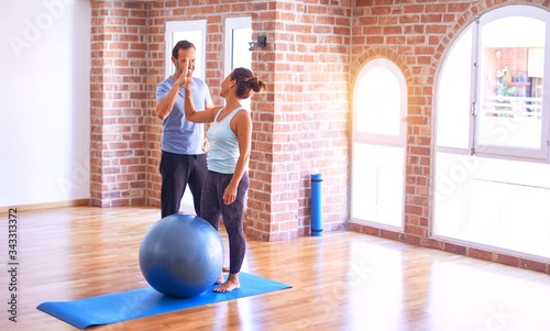 Middle age beautiful sporty couple smiling happy. Standing with smile on face highing five at gym