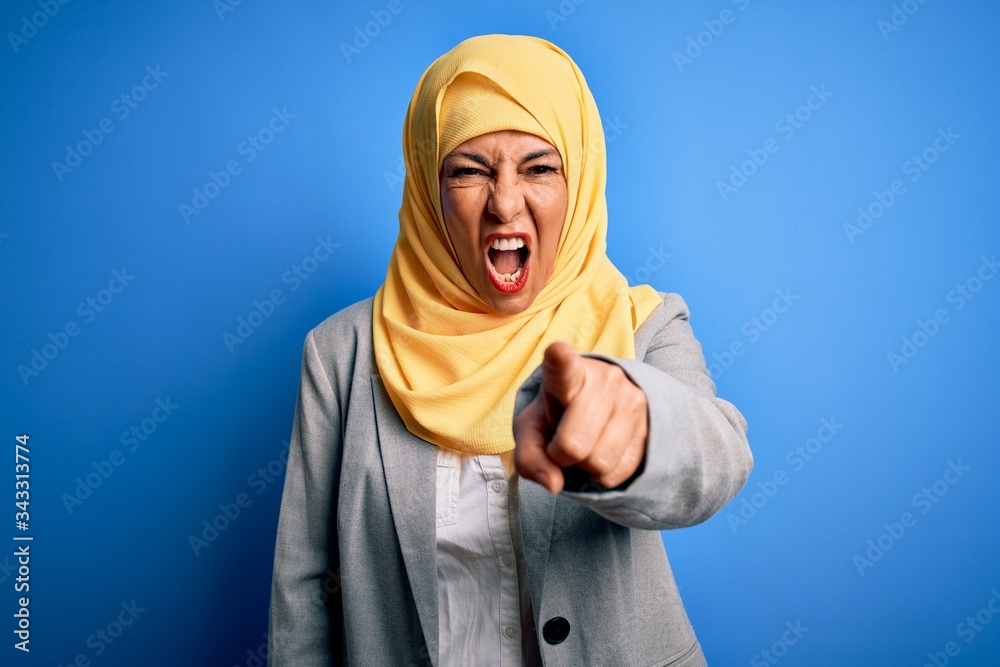 Middle age brunette business woman wearing muslim traditional hijab over blue background pointing displeased and frustrated to the camera, angry and furious with you