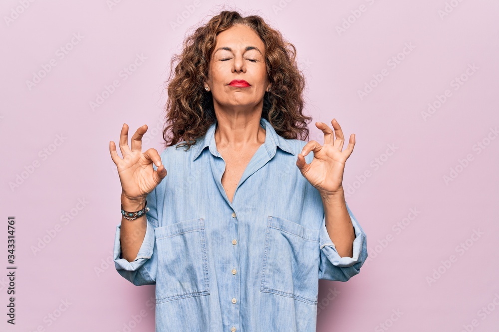 Middle age beautiful woman wearing casual denim shirt standing over pink background relaxed and smiling with eyes closed doing meditation gesture with fingers. Yoga concept. Middle age beautiful woman wearing casual denim shirt standing over pink background relaxed and smiling with eyes closed doing meditation gesture with fingers. Yoga concept.