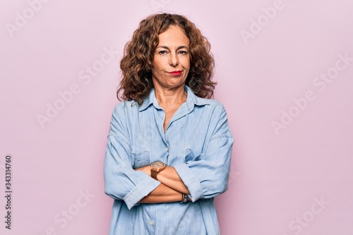Middle age beautiful woman wearing casual denim shirt standing over pink background skeptic and nervous, disapproving expression on face with crossed arms. Negative person.