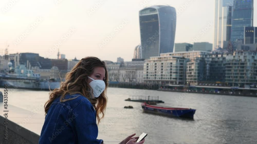 Young woman with face mask outside in city on her phone in London Young woman with face mask outside in city on her phone in London