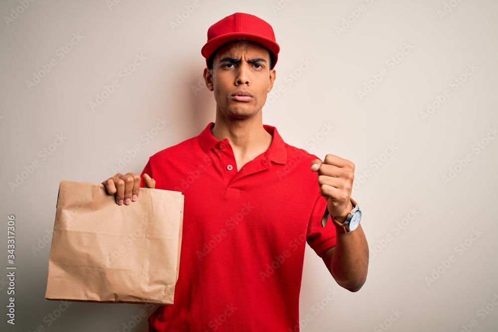 Young handsome african american delivery man holding paper bag with takeaway food annoyed and frustrated shouting with anger, crazy and yelling with raised hand, anger concept