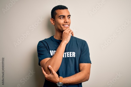 Young handsome african american man volunteering wearing t-shirt with volunteer message with hand on chin thinking about question, pensive expression. Smiling with thoughtful face. Doubt concept.
