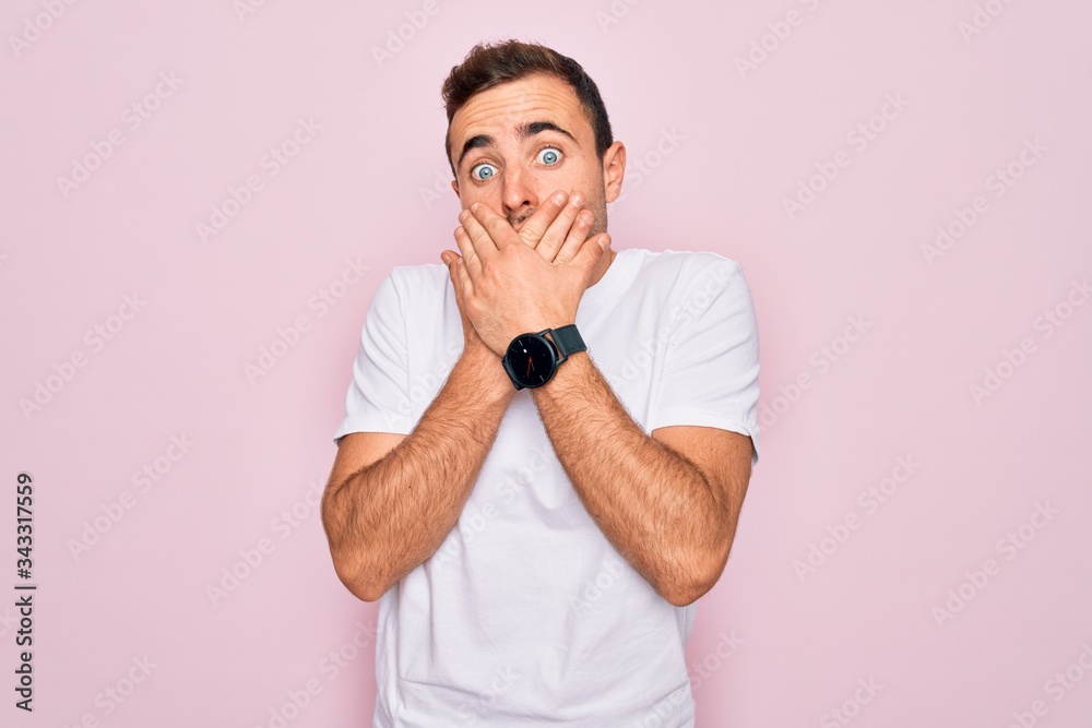 Handsome man with blue eyes wearing casual white t-shirt standing over pink background shocked covering mouth with hands for mistake. Secret concept. Handsome man with blue eyes wearing casual white t-shirt standing over pink background shocked covering mouth with hands for mistake. Secret concept.