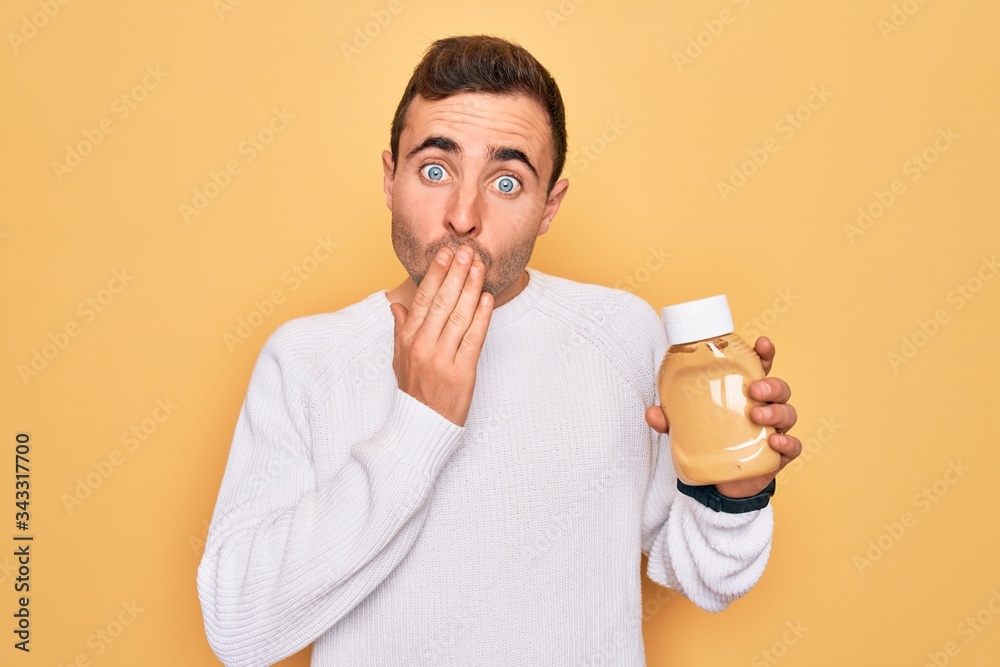 Young handsome man holding bottle of mustard sauce condiment over