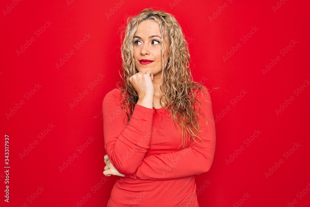 Young beautiful blonde woman wearing red casual t-shirt standing over isolated background with hand on chin thinking about question, pensive expression. Smiling with thoughtful face. Doubt concept. Young beautiful blonde woman wearing red casual t-shirt standing over isolated background with hand on chin thinking about question, pensive expression. Smiling with thoughtful face. Doubt concept.