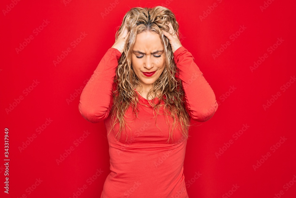 Young beautiful blonde woman wearing red casual t-shirt standing over isolated background with hand on head for pain in head because stress. Suffering migraine. Young beautiful blonde woman wearing red casual t-shirt standing over isolated background with hand on head for pain in head because stress. Suffering migraine.