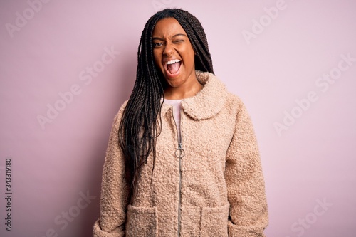 Young african american woman wearing fashion winter coat over pink isolated background winking looking at the camera with sexy expression, cheerful and happy face. © Krakenimages.com