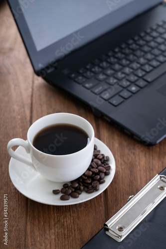  Black coffee in a white coffee mug on top and a notebook on a wooden table, wooden table