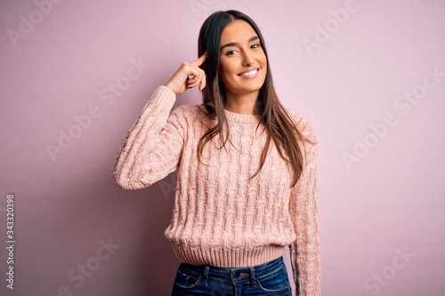 Young beautiful brunette woman wearing casual sweater over isolated pink background Smiling pointing to head with one finger, great idea or thought, good memory