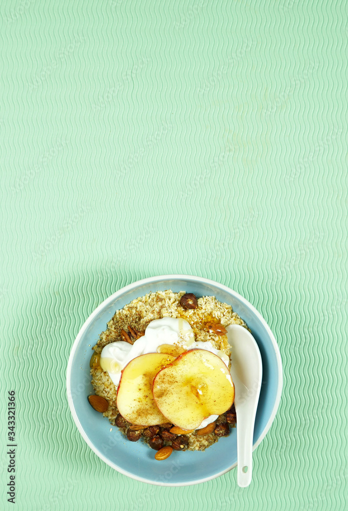 Healthy breakfast bowl with oats, spices, yogurt, fresh fruit, nuts, honey and high fiber LSA on modern green background. Top view flatlay with negative copy space. Vertical. Healthy breakfast bowl with oats, spices, yogurt, fresh fruit, nuts, honey and high fiber LSA on modern green background. Top view flatlay with negative copy space. Vertical.