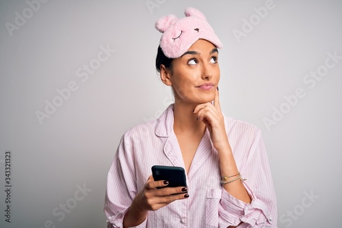 Young beautiful woman wearing pajama and sleep mask having conversation using smartphone serious face thinking about question, very confused idea © Krakenimages.com