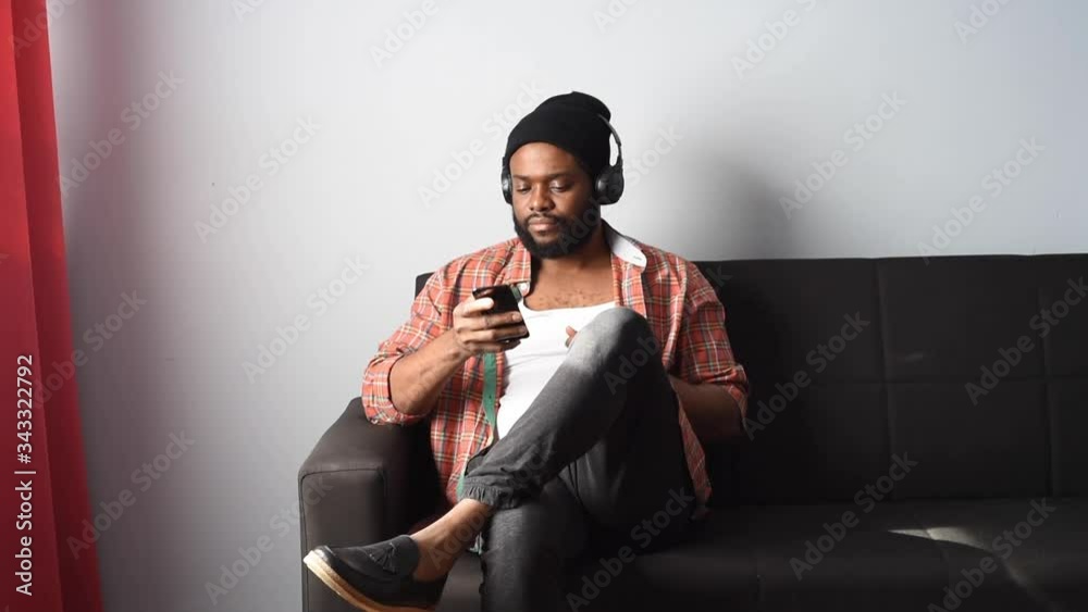 A handsome black man wearing a black hat and headphones, listening to music. An African American man dancing to music from his headphone. head and body movements. mood vibes! A handsome black man wearing a black hat and headphones, listening to music. An African American man dancing to music from his headphone. head and body movements. mood vibes!