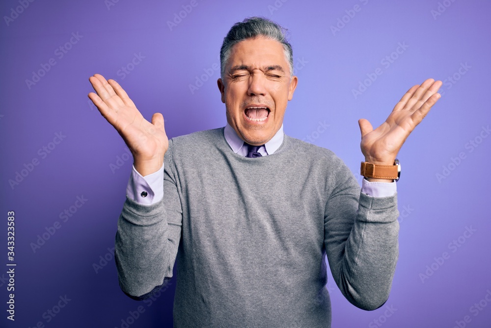 Middle age handsome grey-haired man wearing elegant sweater over purple background celebrating mad and crazy for success with arms raised and closed eyes screaming excited. Winner concept Middle age handsome grey-haired man wearing elegant sweater over purple background celebrating mad and crazy for success with arms raised and closed eyes screaming excited. Winner concept