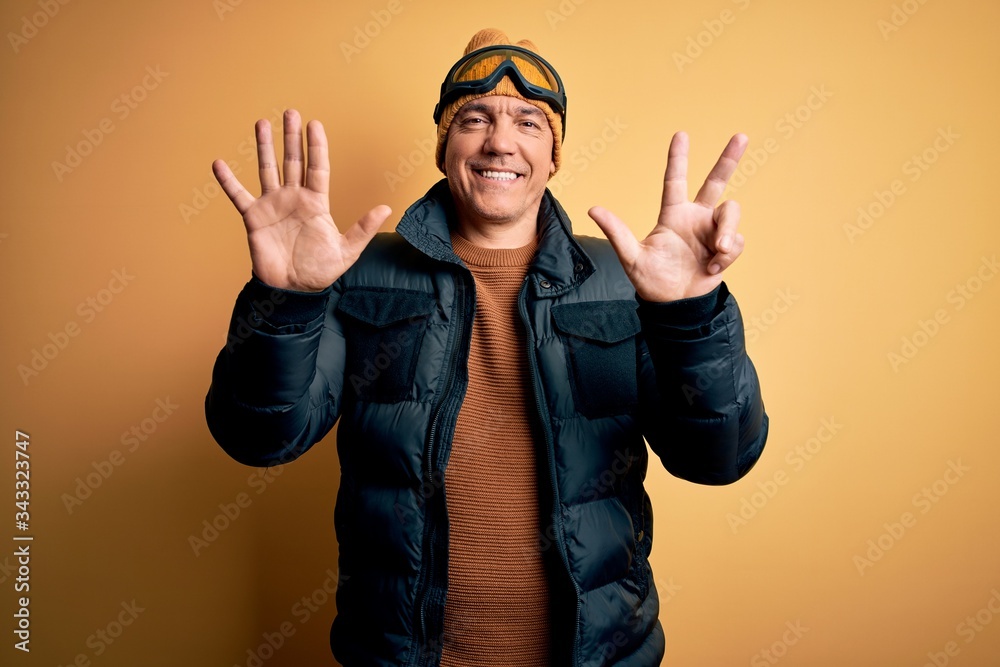 Middle age handsome grey-haired skier man on vacation wearing ski goggles showing and pointing up with fingers number eight while smiling confident and happy.