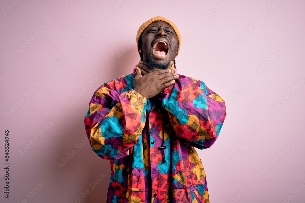 Obraz premium Young handsome african american man wearing colorful coat and cap over pink background shouting and suffocate because painful strangle. Health problem. Asphyxiate and suicide concept.