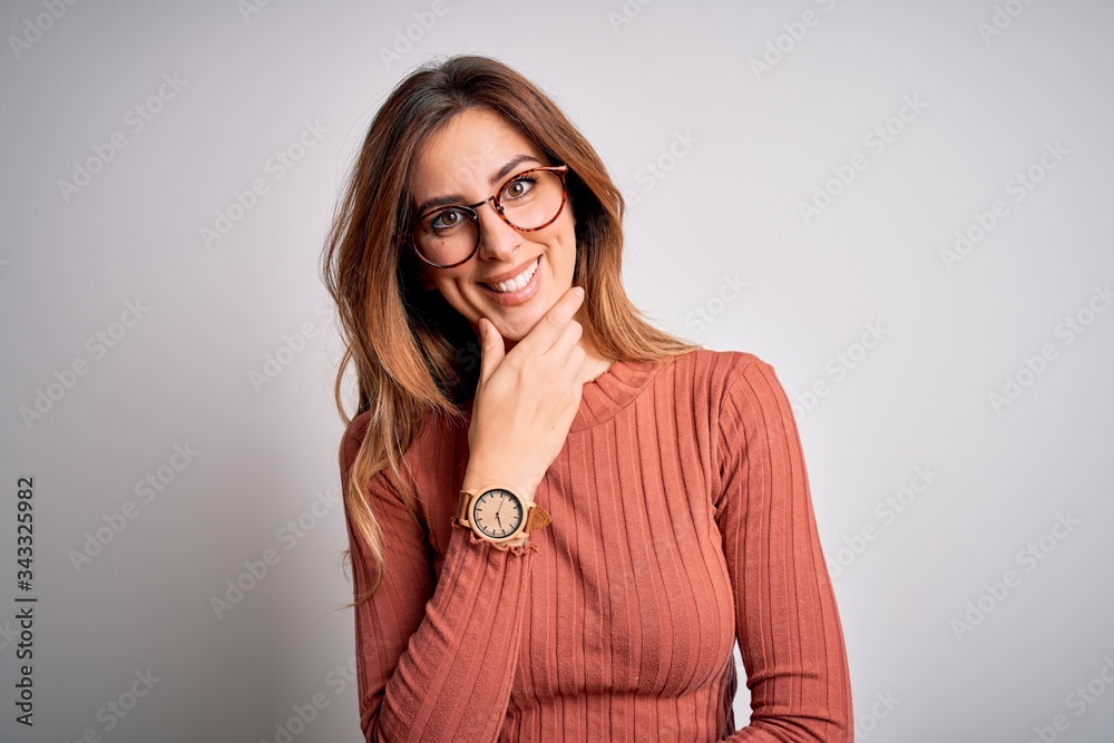 Young beautiful brunette woman wearing casual sweater and glasses over white background looking confident at the camera smiling with crossed arms and hand raised on chin. Thinking positive. Young beautiful brunette woman wearing casual sweater and glasses over white background looking confident at the camera smiling with crossed arms and hand raised on chin. Thinking positive.