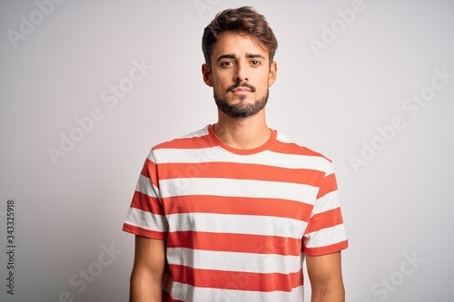 Young handsome man with beard wearing striped t-shirt standing over white background Relaxed with serious expression on face. Simple and natural looking at the camera.