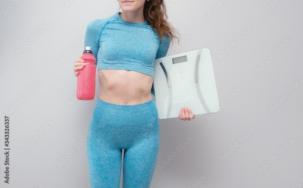 Slim girl with scales isolated on grey costume. Concept of loosing weight, workout, home training. Slim girl with scales isolated on grey costume. Concept of loosing weight, workout, home training.