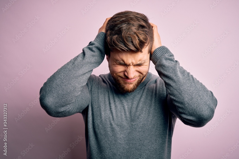 Young handsome blond man with beard and blue eyes wearing casual sweater suffering from headache desperate and stressed because pain and migraine. Hands on head. Young handsome blond man with beard and blue eyes wearing casual sweater suffering from headache desperate and stressed because pain and migraine. Hands on head.