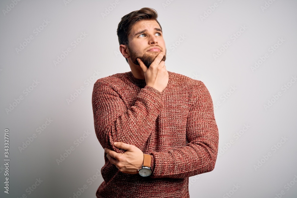 Young blond man with beard and blue eyes wearing casual sweater over white background with hand on chin thinking about question, pensive expression. Smiling with thoughtful face. Doubt concept. Young blond man with beard and blue eyes wearing casual sweater over white background with hand on chin thinking about question, pensive expression. Smiling with thoughtful face. Doubt concept.