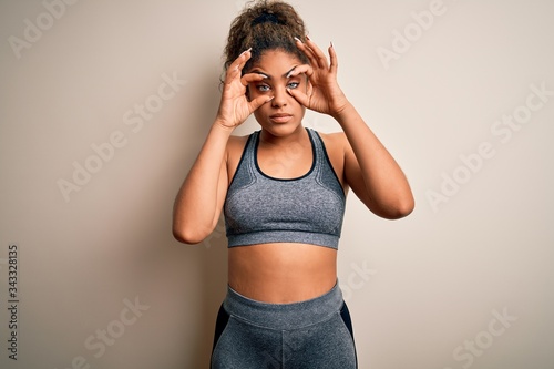 Young african american sportswoman doing sport wearing sportswear over white background Trying to open eyes with fingers, sleepy and tired for morning fatigue