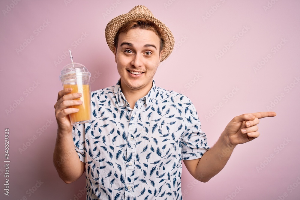 Young handsome redhead man on vacation drinking glass of healthy orange juice Smiling happy pointing with hand and finger to the side Young handsome redhead man on vacation drinking glass of healthy orange juice Smiling happy pointing with hand and finger to the side