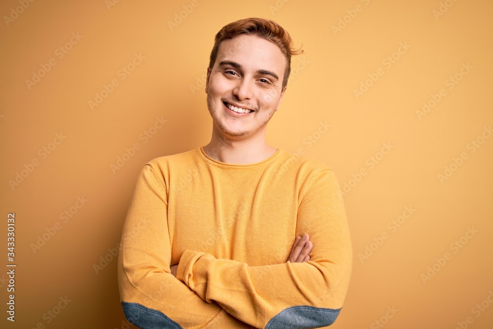 Young handsome redhead man wearing casual sweater over isolated yellow background happy face smiling with crossed arms looking at the camera. Positive person.