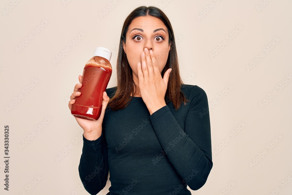 Φωτογραφία Young beautiful brunette woman holding bottle with ketchup sauce over white background covering mouth with hand, shocked and afraid for mistake