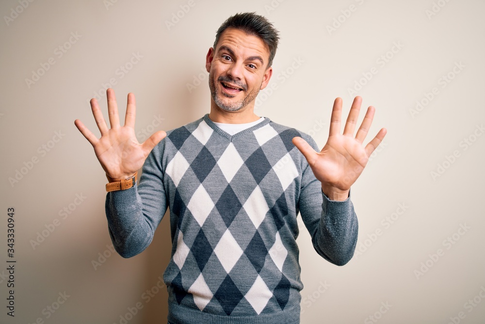 Young handsome man wearing casual sweater standing over isolated white background showing and pointing up with fingers number ten while smiling confident and happy. Young handsome man wearing casual sweater standing over isolated white background showing and pointing up with fingers number ten while smiling confident and happy.