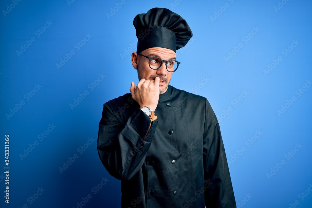 Young handsome chef man wearing cooker uniform and hat over isolated blue background looking stressed and nervous with hands on mouth biting nails. Anxiety problem.