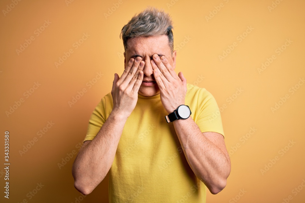 Young handsome modern man wearing yellow shirt over yellow isolated background rubbing eyes for fatigue and headache, sleepy and tired expression. Vision problem Young handsome modern man wearing yellow shirt over yellow isolated background rubbing eyes for fatigue and headache, sleepy and tired expression. Vision problem