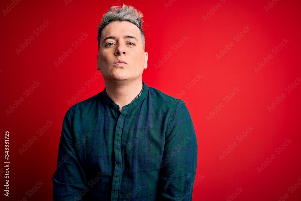 Obraz premium Young handsome modern man wearing elegant green shirt over red isolated background looking at the camera blowing a kiss on air being lovely and sexy. Love expression.