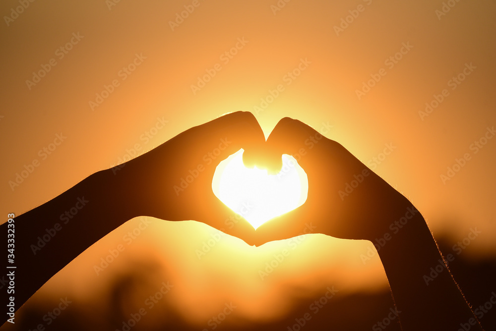Silhouette hand made heart shape on the sunset background. Send love for the person you love Concept.