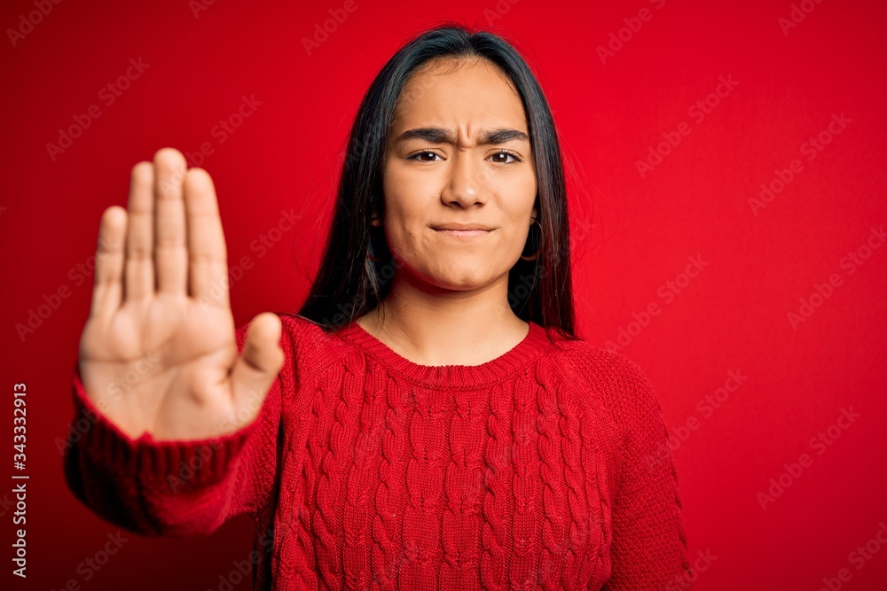 Young beautiful asian woman wearing casual sweater standing over isolated red background doing stop sing with palm of the hand. Warning expression with negative and serious gesture on the face. Young beautiful asian woman wearing casual sweater standing over isolated red background doing stop sing with palm of the hand. Warning expression with negative and serious gesture on the face.